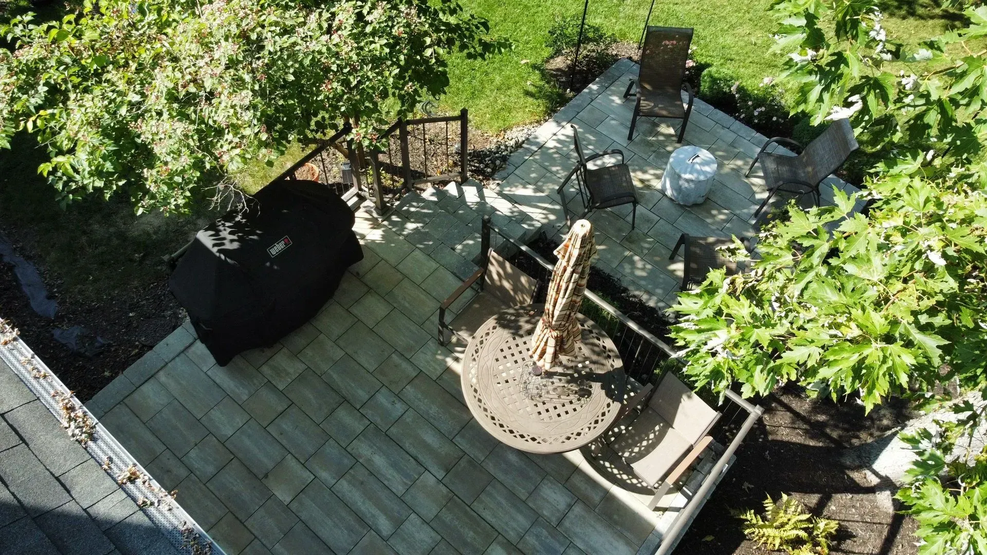 Backyard patio with wicker chair, round table, and garden surrounded by greenery