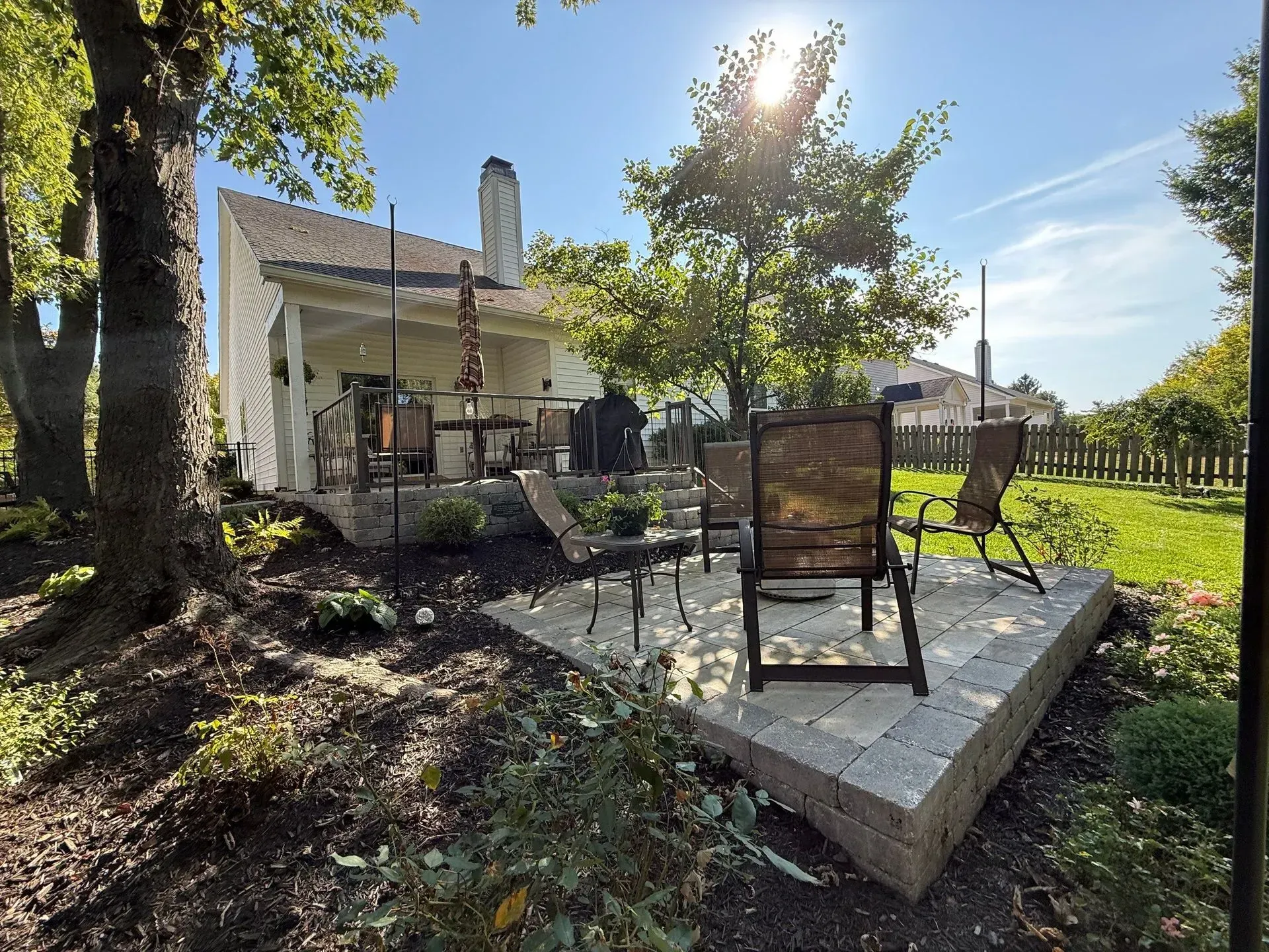 Patio with metal chairs and table on a raised stone platform in a sunny backyard garden
