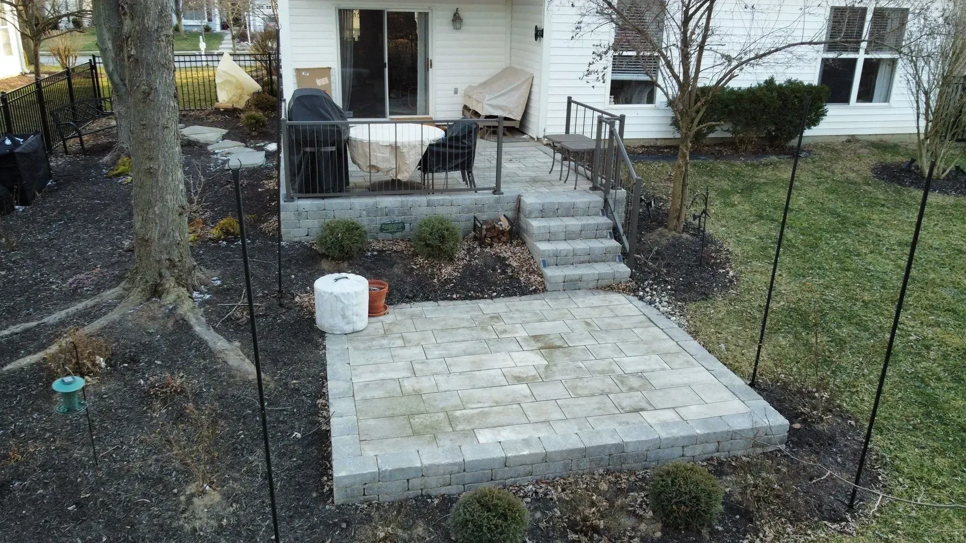 Backyard patio with stone steps, black metal fence, and a house in the background
