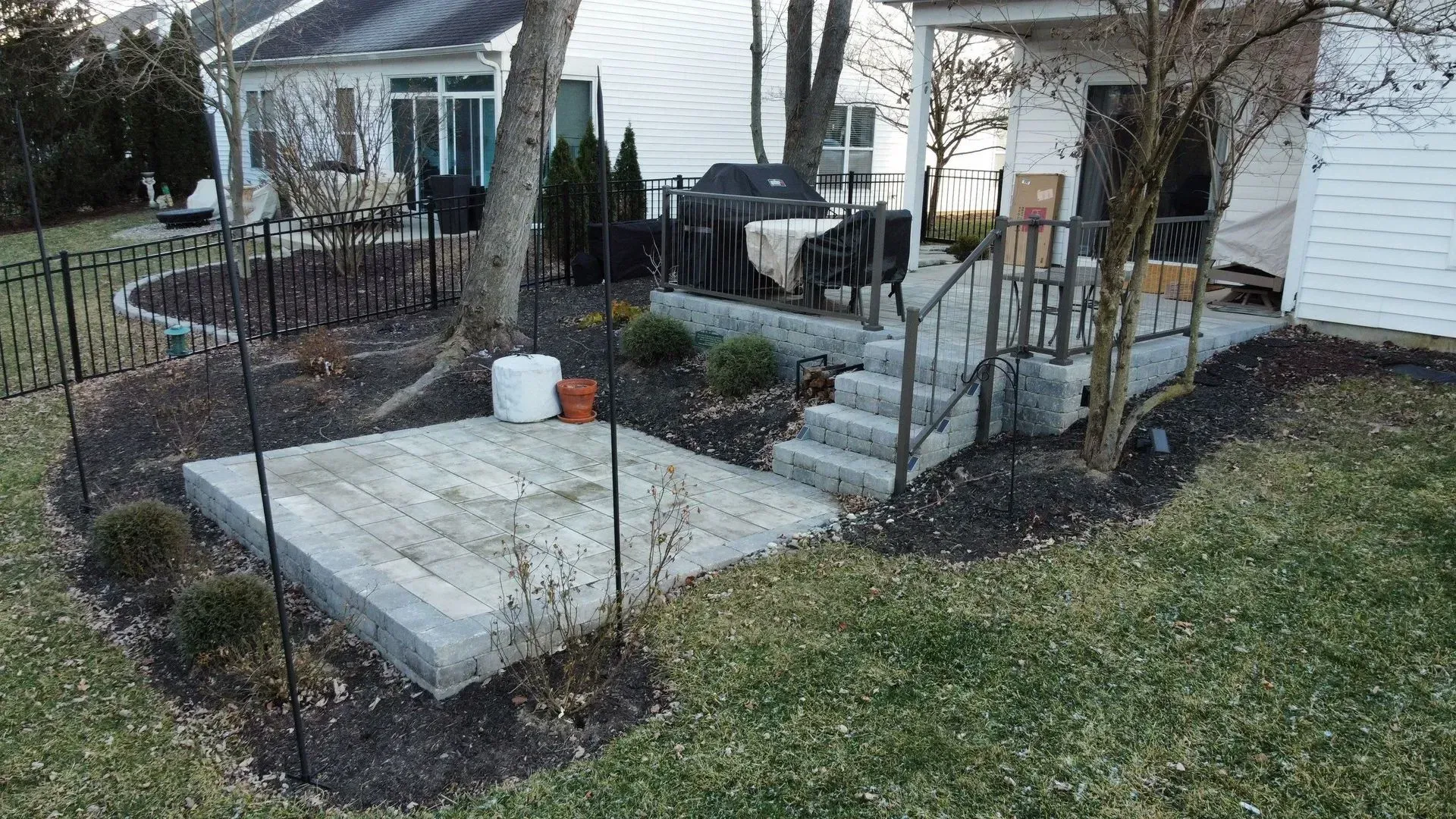 Small front yard patio with concrete steps, black railings, and potted plants beside a white house
