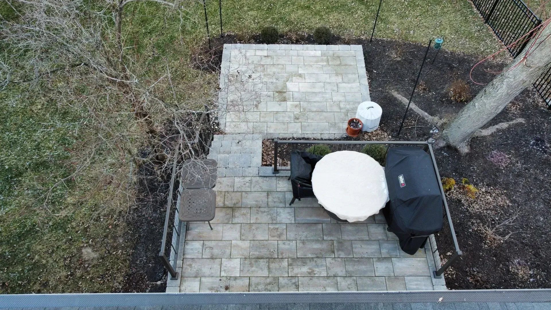 Overhead view of a small backyard patio with white and gray paving stones, a grill, and a round table.