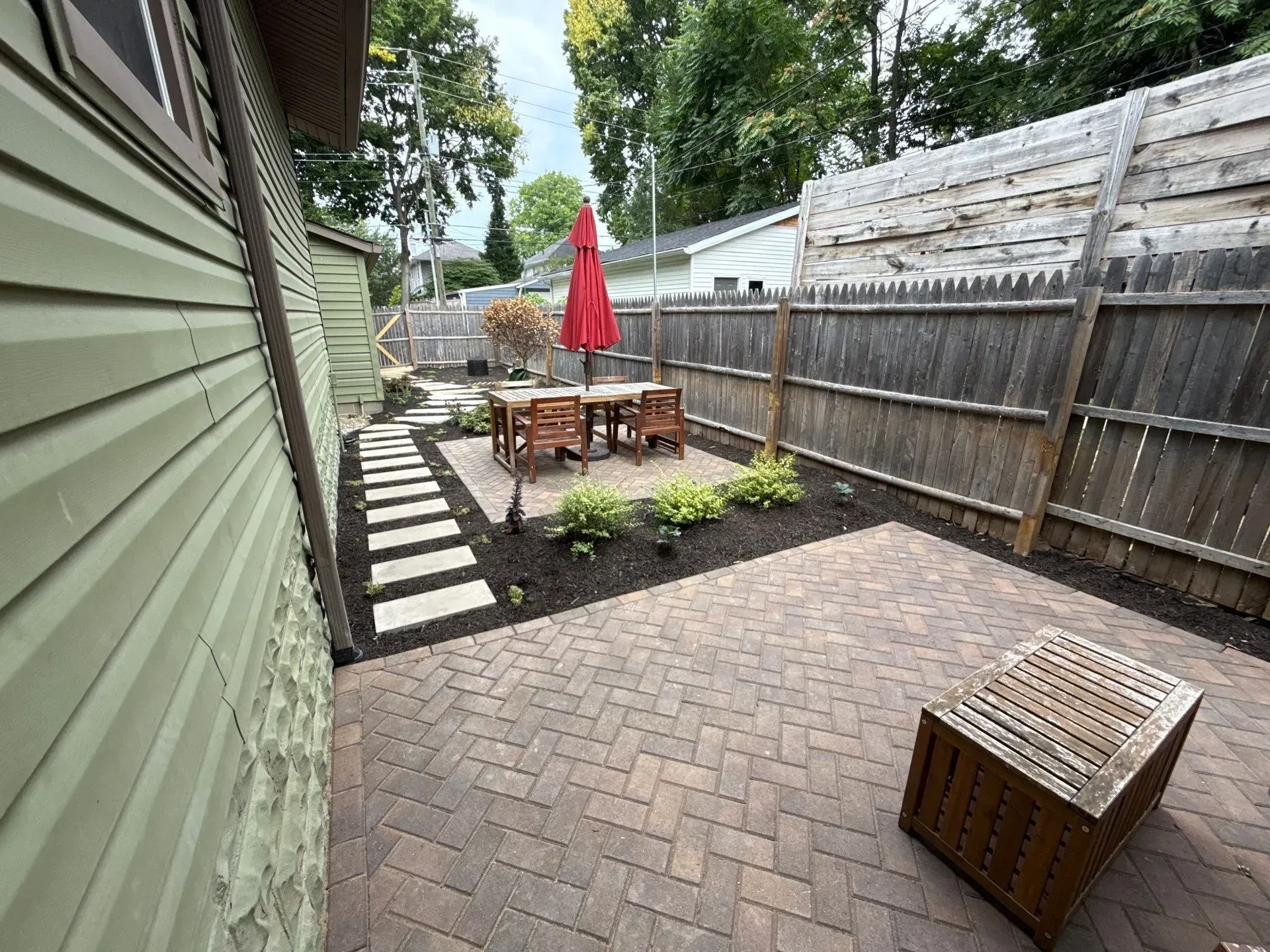 Backyard patio with brick pavers, wooden fence, red umbrella, and outdoor table set