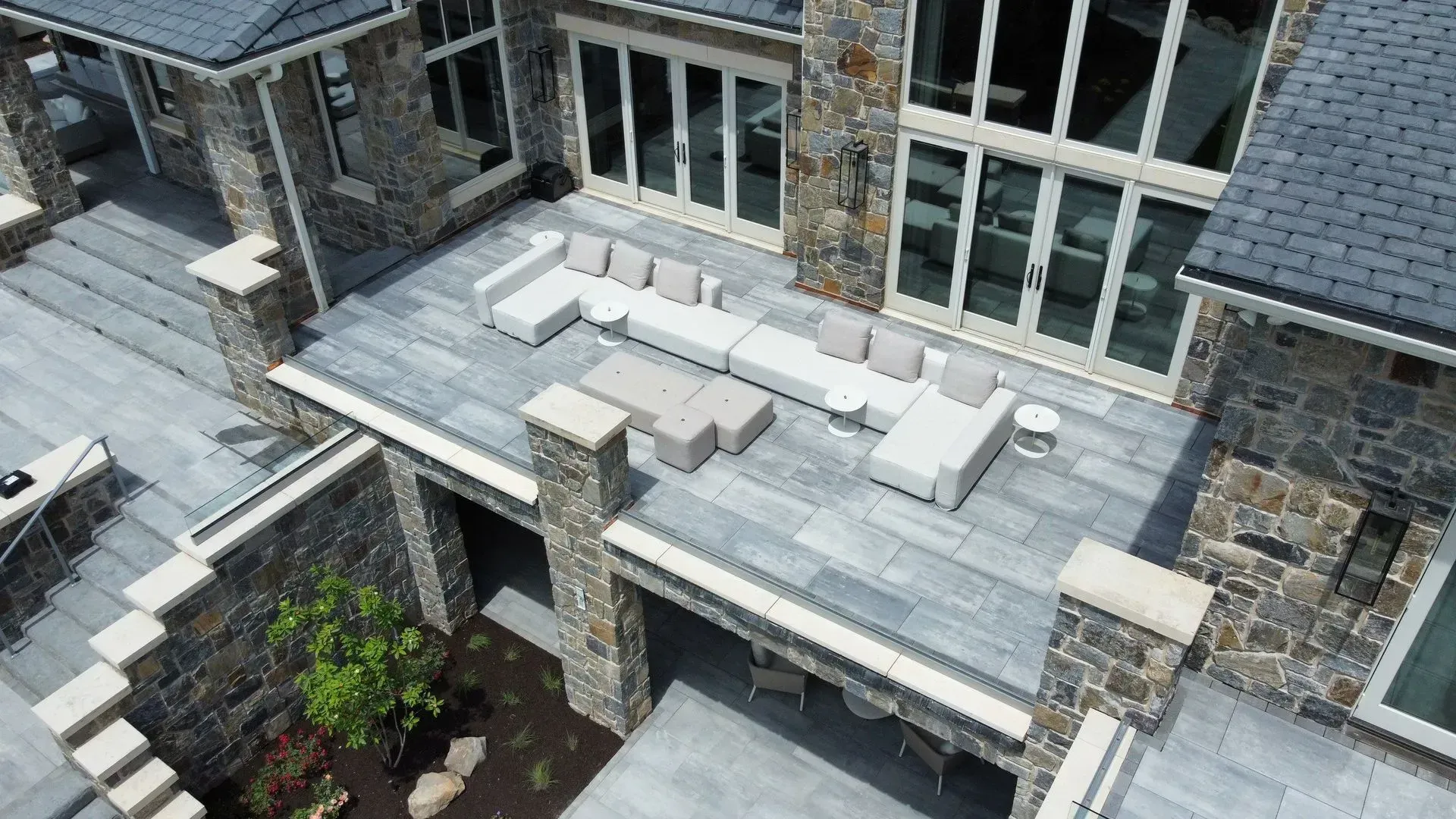 Stone house rooftop patio with gray tile, white lounge furniture, and windows overlooking a courtyard