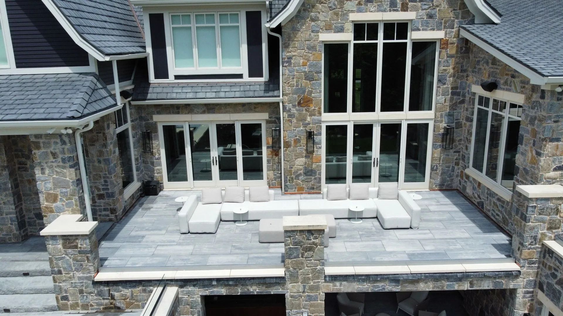 Stone patio with white outdoor furniture on a luxury house terrace overlooking tall windows