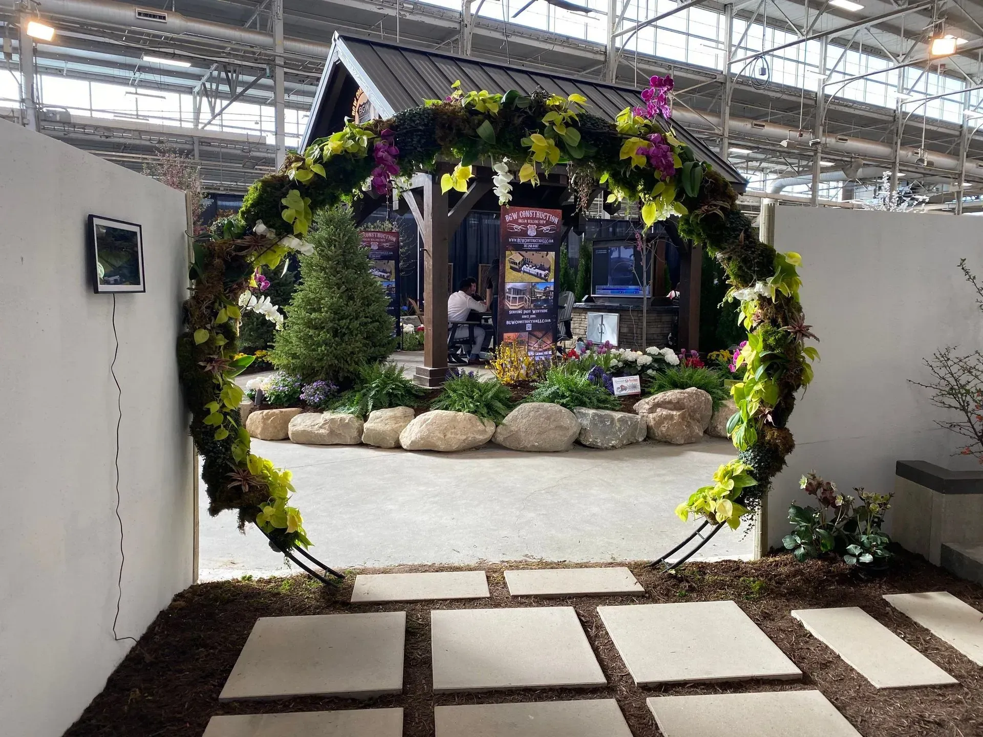 Flower-covered circular archway in a garden display with stepping stones leading through it