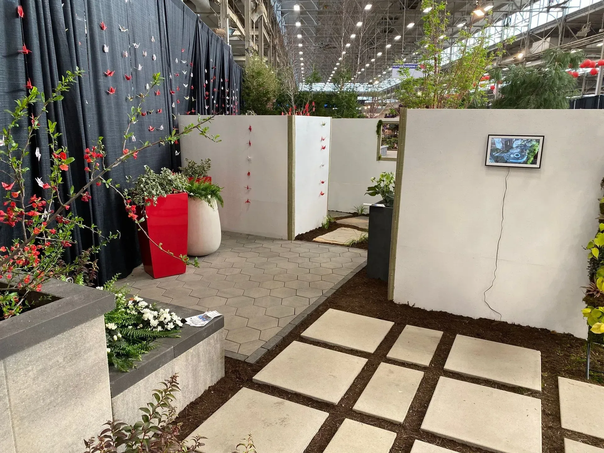 Indoor garden walkway with white walls, potted plants, and a tiled path under a glass roof