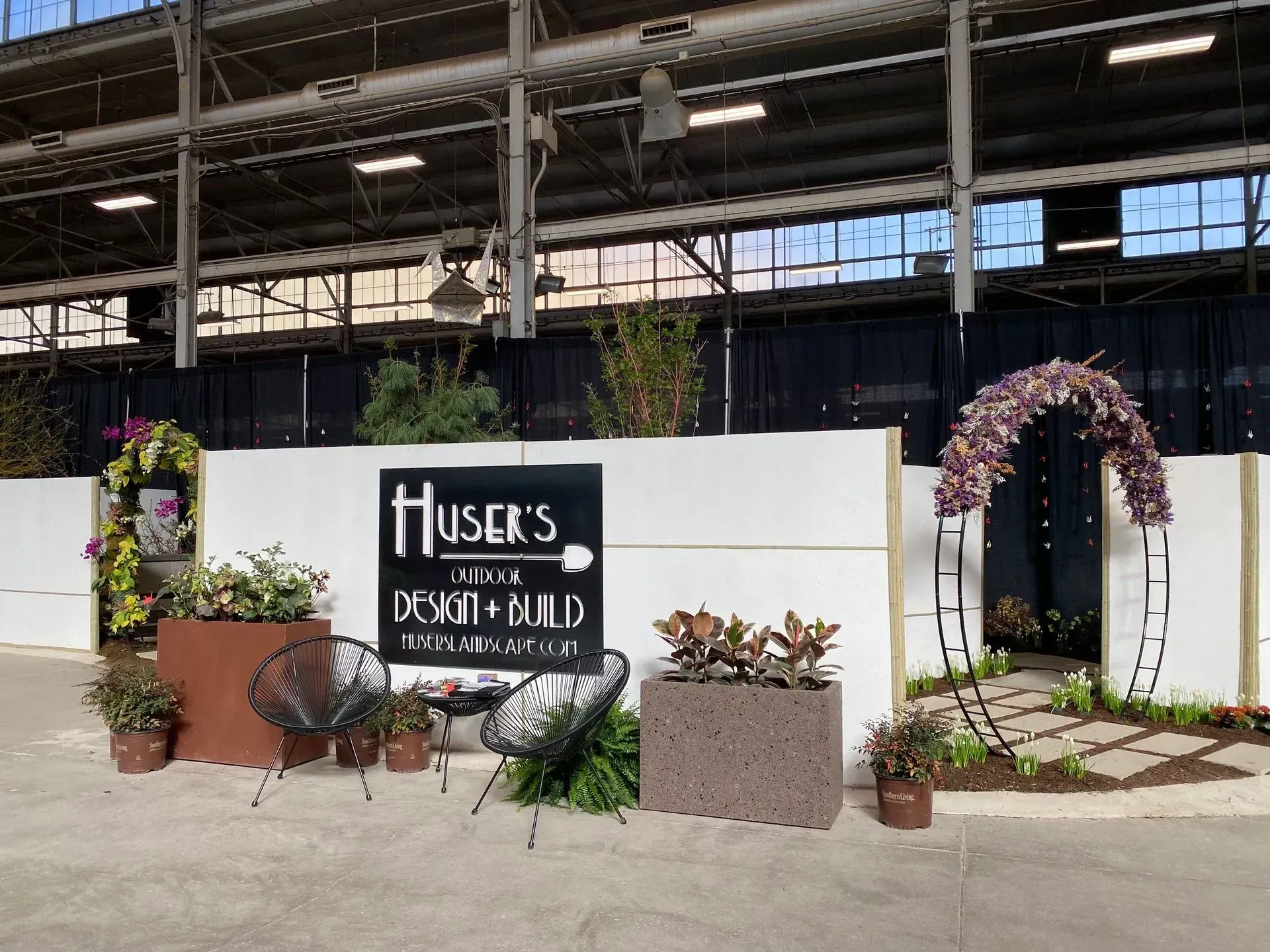 Flower-filled memorial display with a black sign and pink floral arch against a white wall