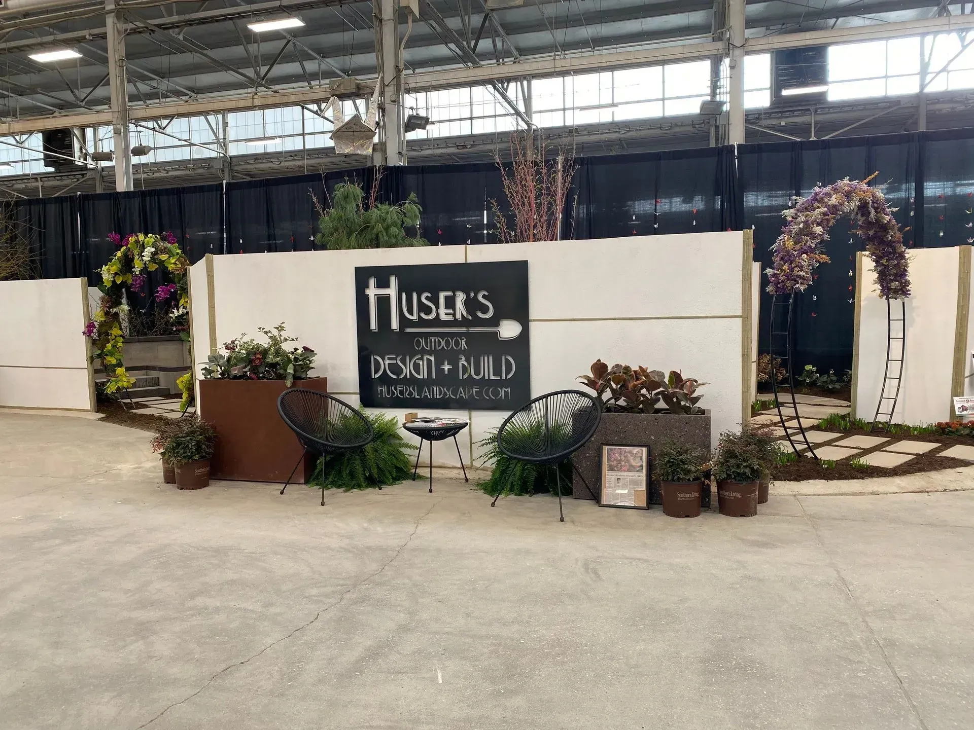 Booth with “Husker” sign, potted plants, and tables in an indoor greenhouse setting