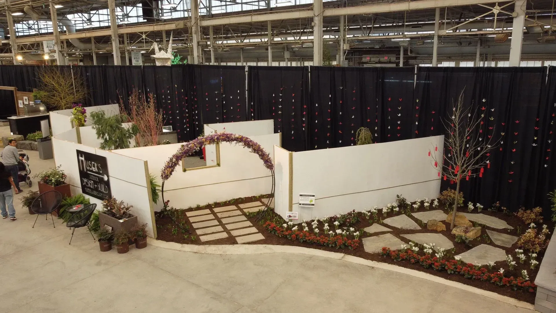 Indoor garden display with white walls, flower beds, archway, and stone path on a checkered floor