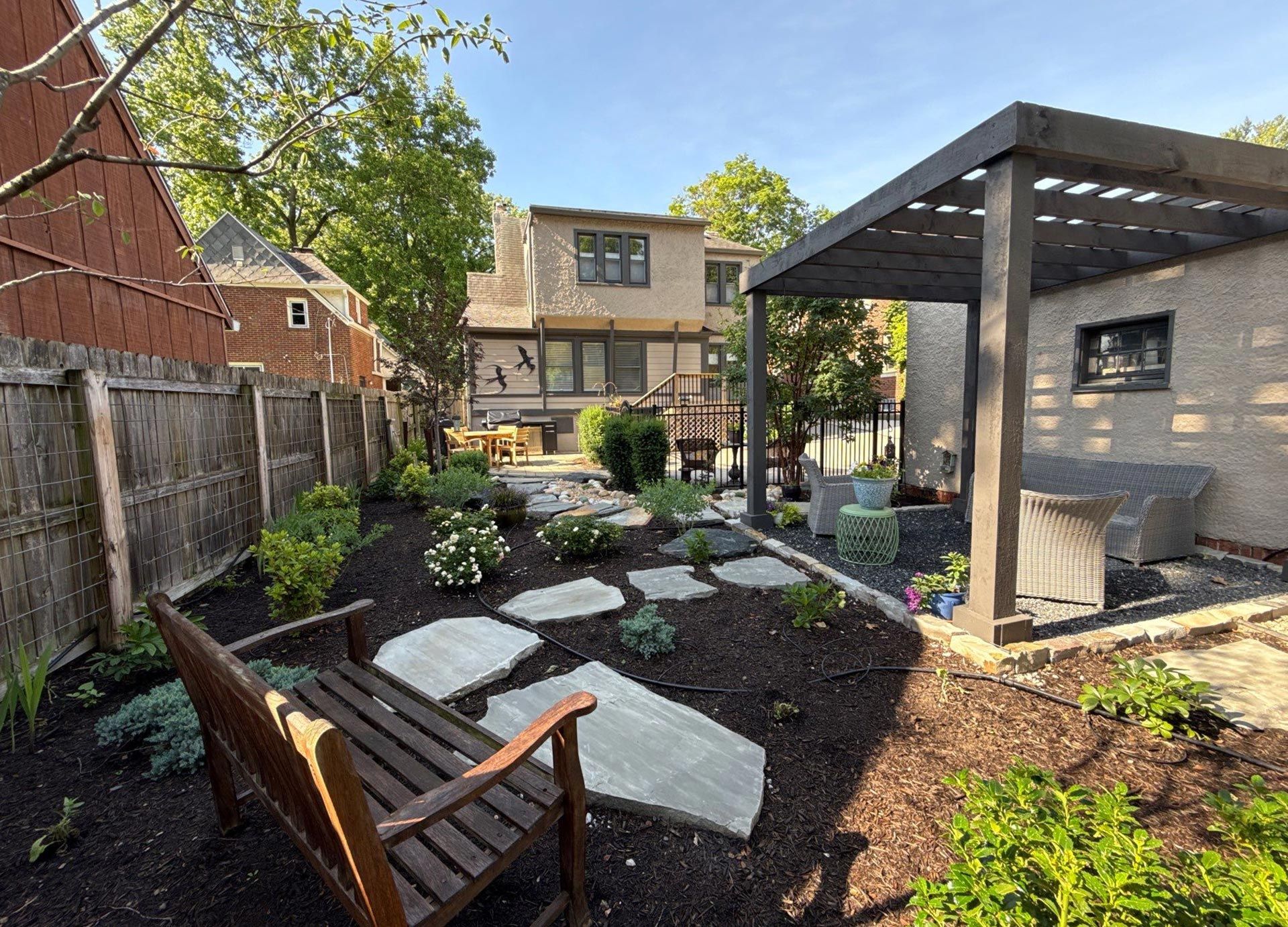 Backyard with garden beds, stepping stones, wooden bench, and pergola.