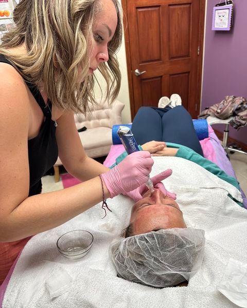 A woman wearing pink gloves is working on a woman's face
