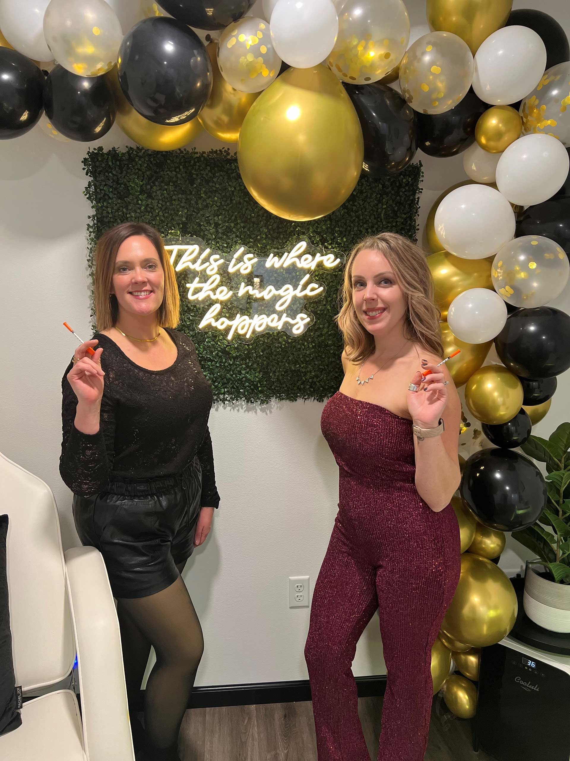 Two women are standing next to each other in front of a wall of balloons
