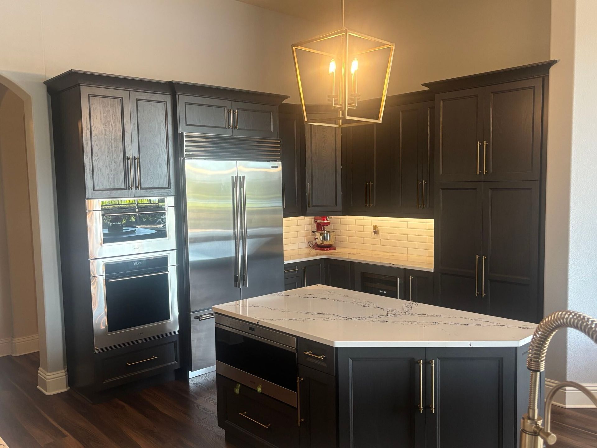 Dark-painted kitchen with stainless steel appliances, a white countertop island, and a gold geometric light fixture.