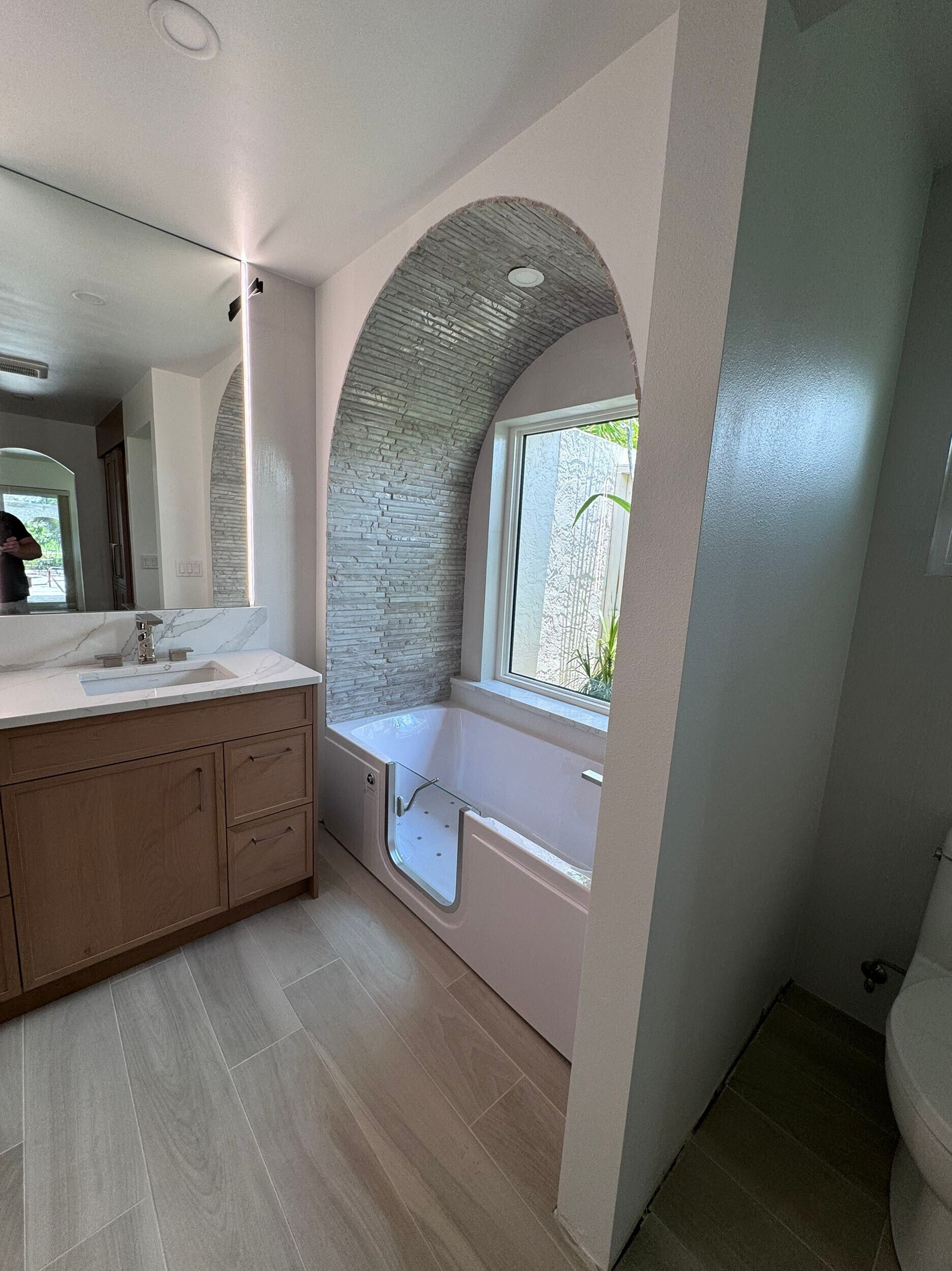 A bathroom with a tub, sink, mirror, and window.