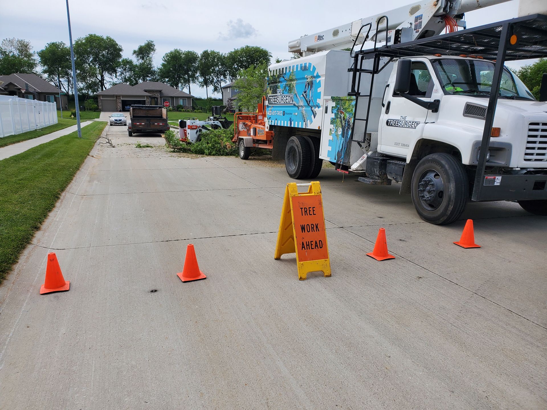 Street scene with tree trimming equipment. Orange cones, a truck, and a caution sign on the road.
