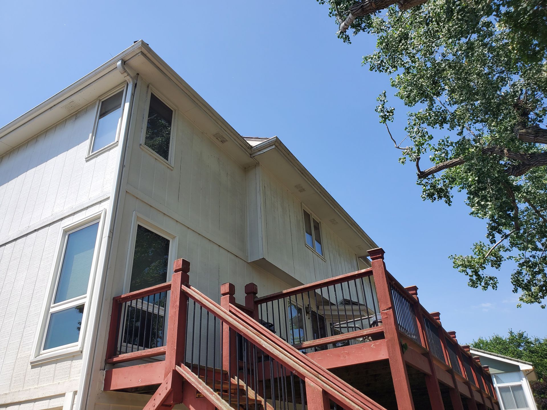 Two-story cream house with a red deck and stairs; blue sky.