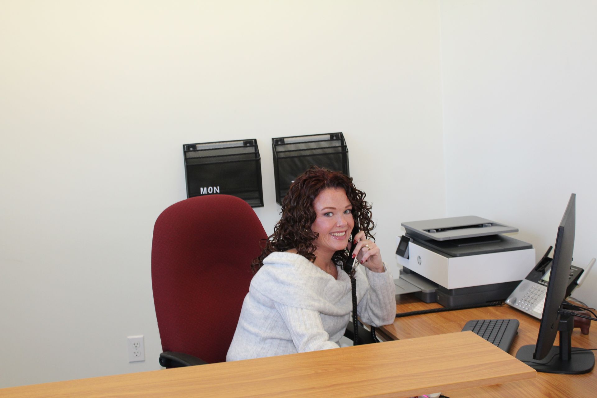 Woman seated at a desk, smiling while on the phone, office setting.