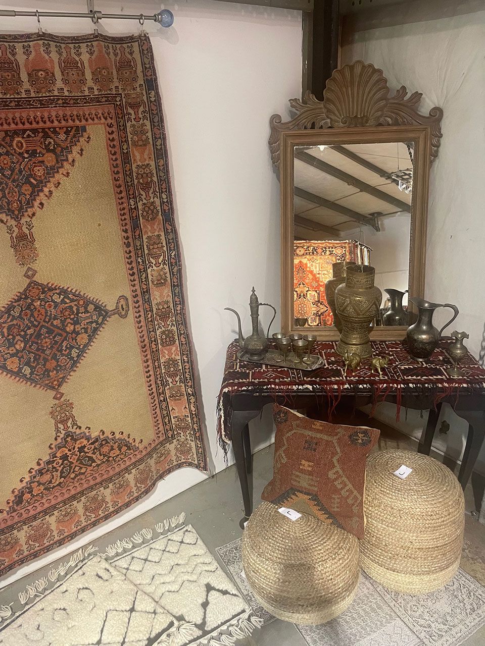 A room with a rug, mirror, table, and vases