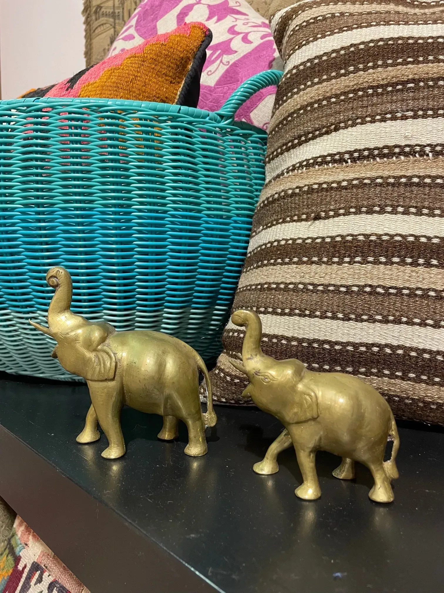 Two gold elephant figurines are sitting on a shelf next to a blue basket.