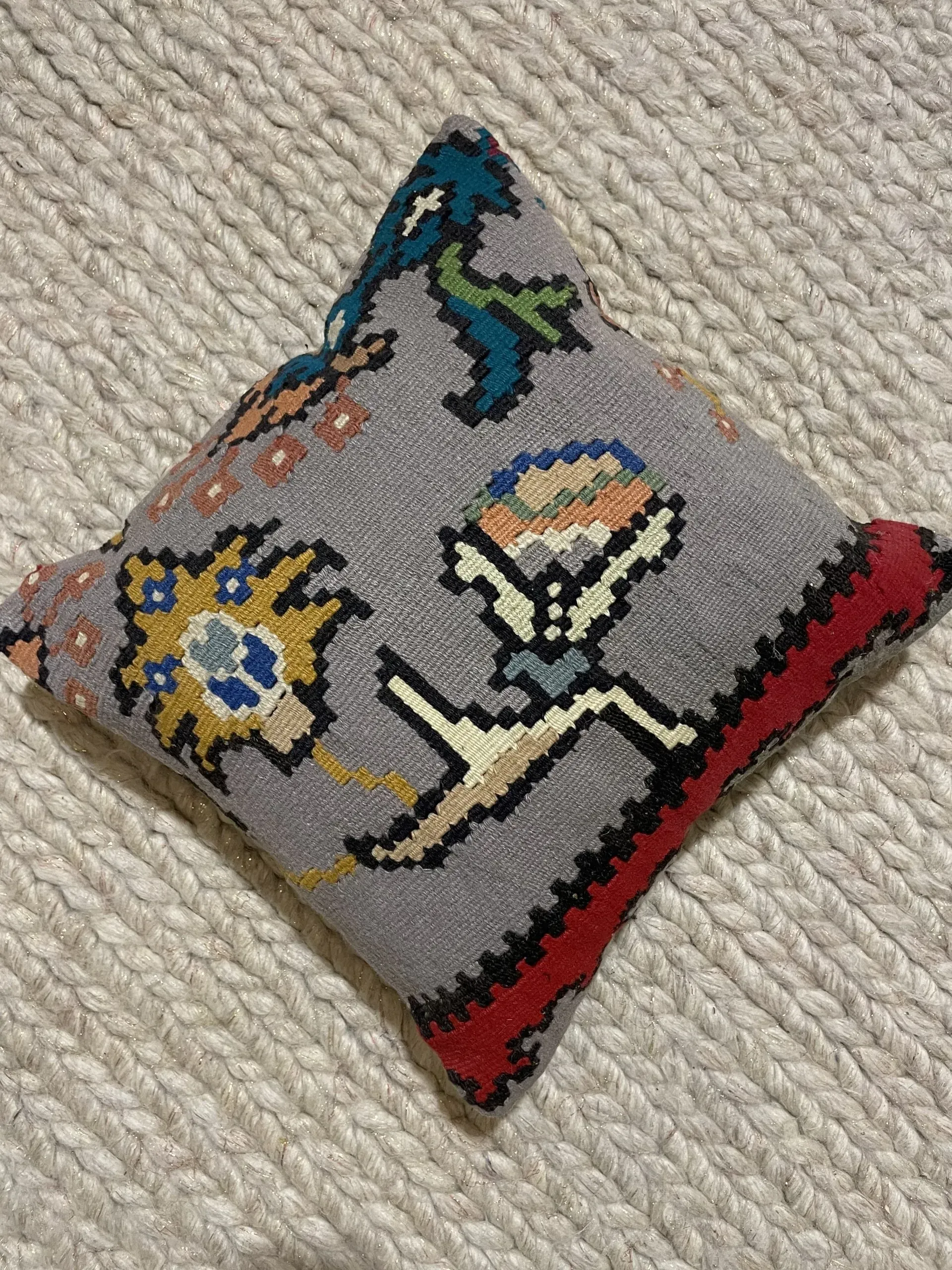A small embroidered pillow is sitting on a white rug.