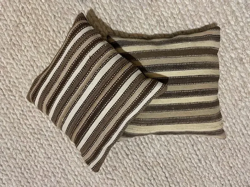 Two striped pillows are stacked on top of each other on a carpet.