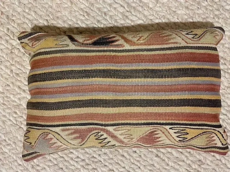 A colorful striped pillow is sitting on a white rug.