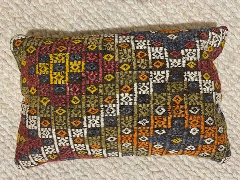 A pillow with a colorful pattern on it is sitting on a white carpet.