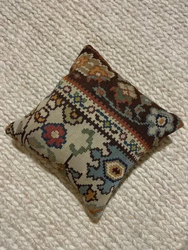 A small pillow with a floral pattern is sitting on a white blanket.