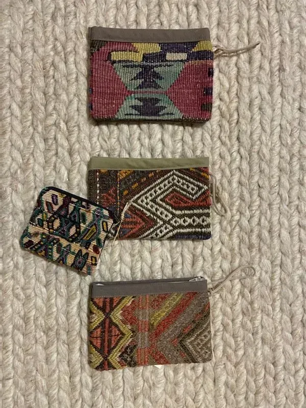 Three colorful wallets are sitting on top of a knitted rug.