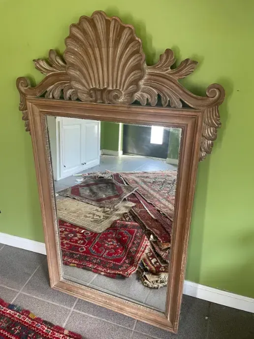 A large mirror with a wooden frame is sitting in a room next to a rug.