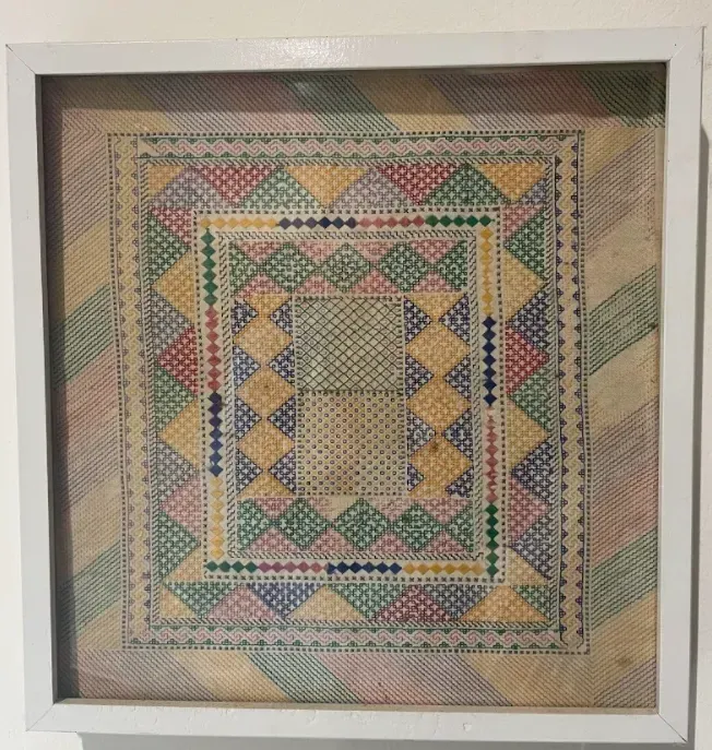 A cross stitch pattern in a white frame on a wall.