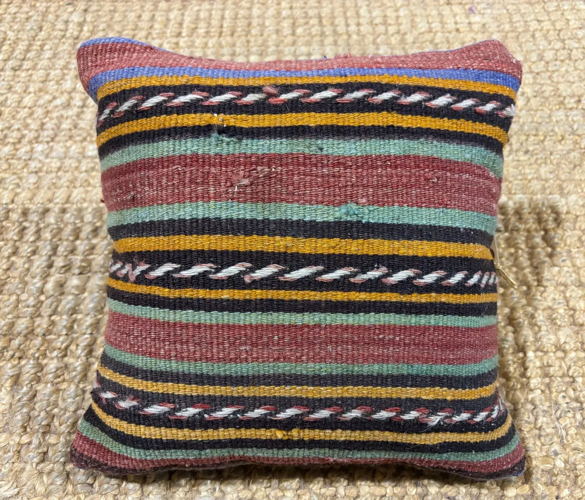 A colorful striped pillow is sitting on top of a jute rug.