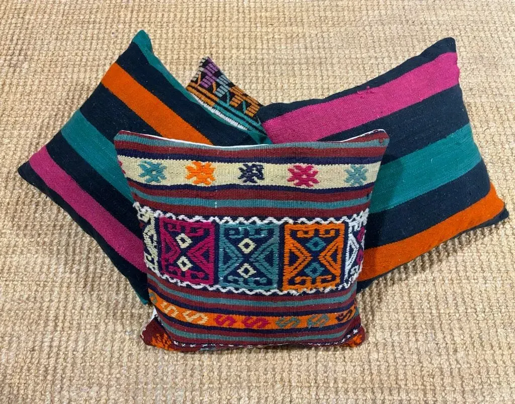 Three colorful pillows are stacked on top of each other on a rug.