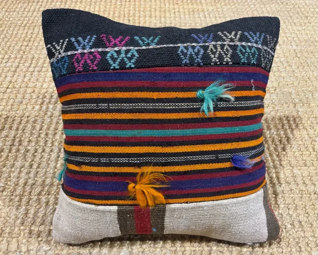 A colorful striped pillow is sitting on a rug.