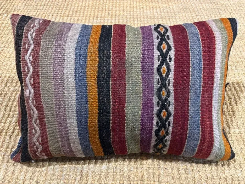 A colorful striped pillow is sitting on a carpet.