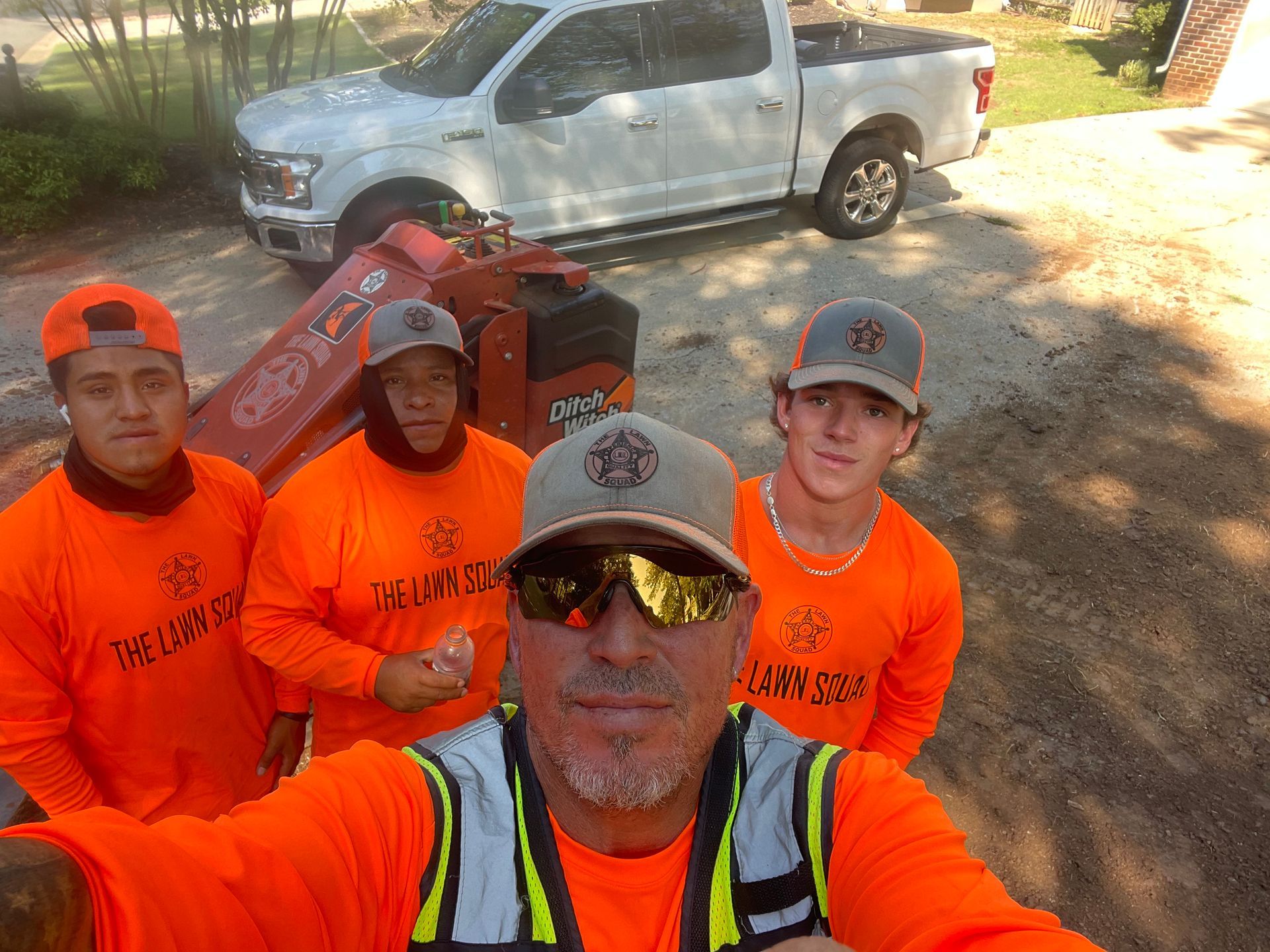 A group of men in orange shirts are standing in front of a white truck.