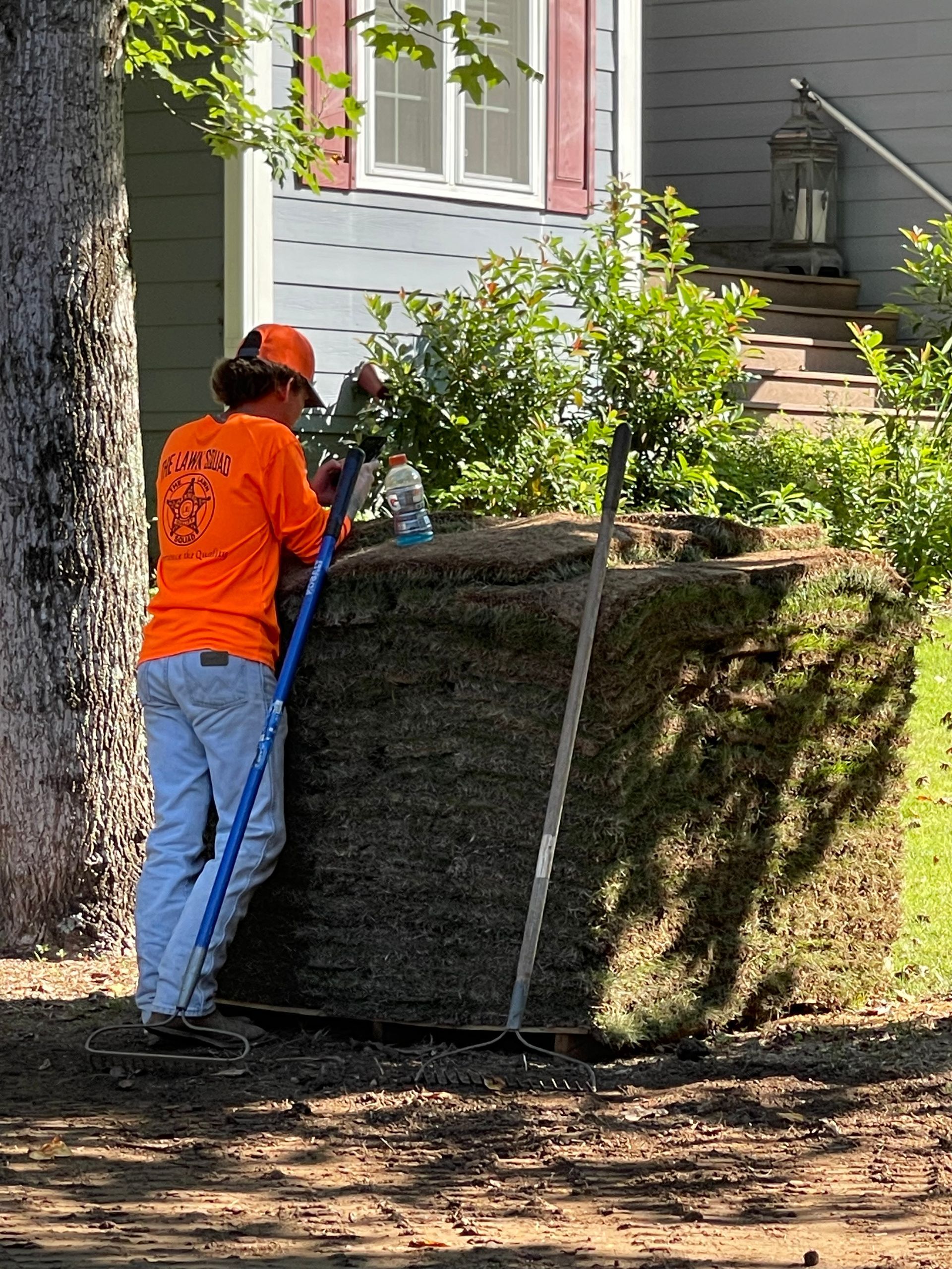 A man is raking a pile of grass in front of a house.
