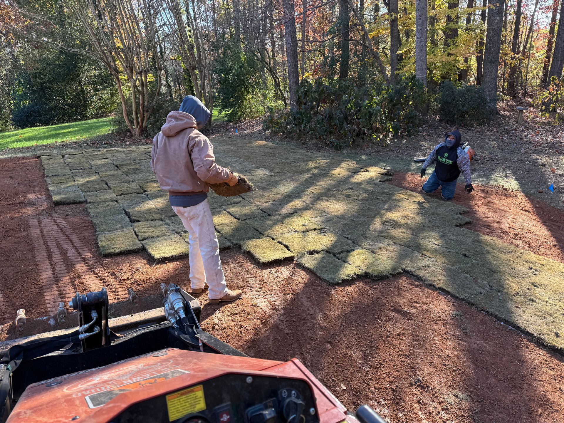 A man is standing next to a tractor while another man is kneeling on the ground.