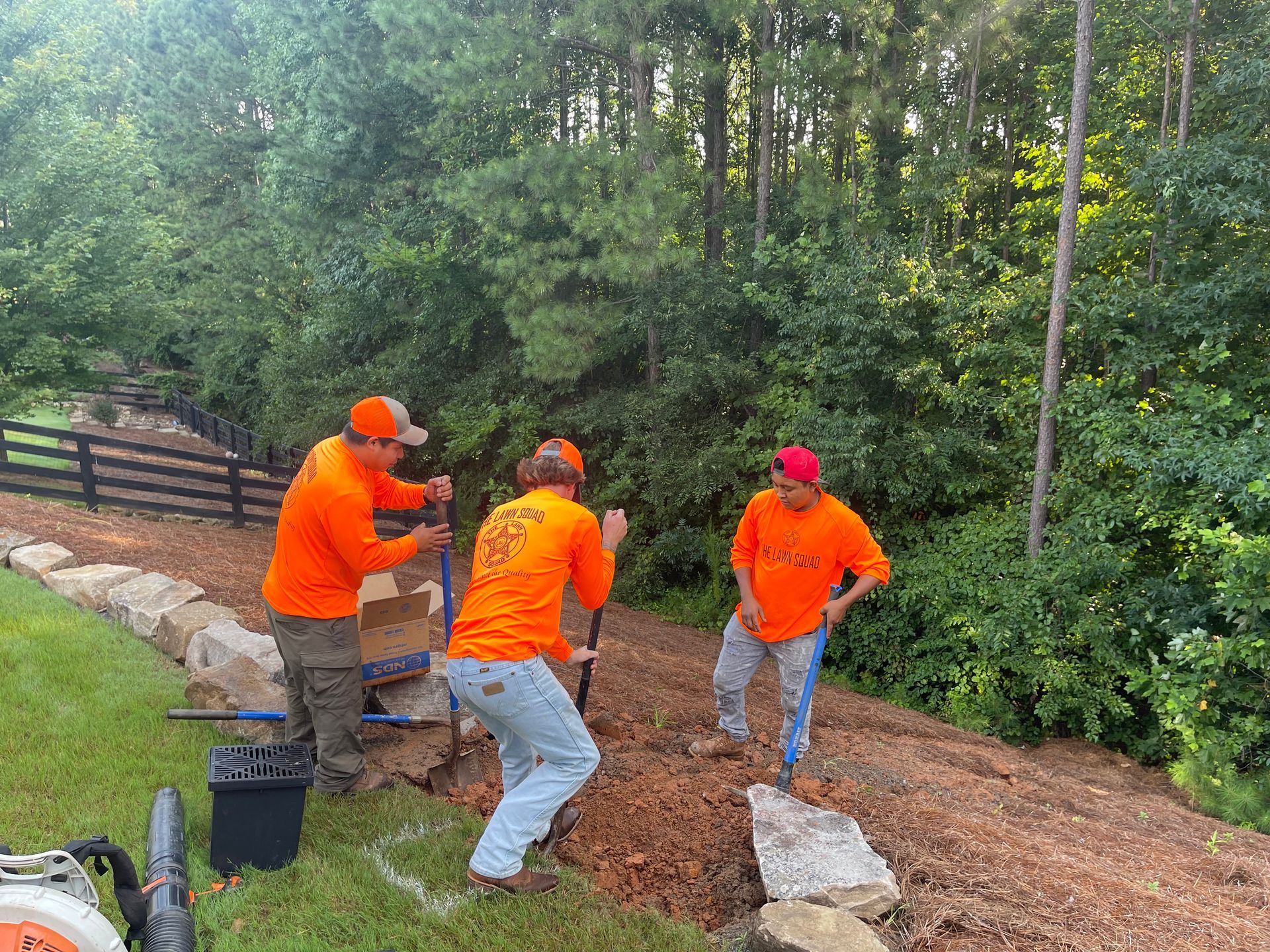 A group of men in orange shirts are digging a hole in the ground.