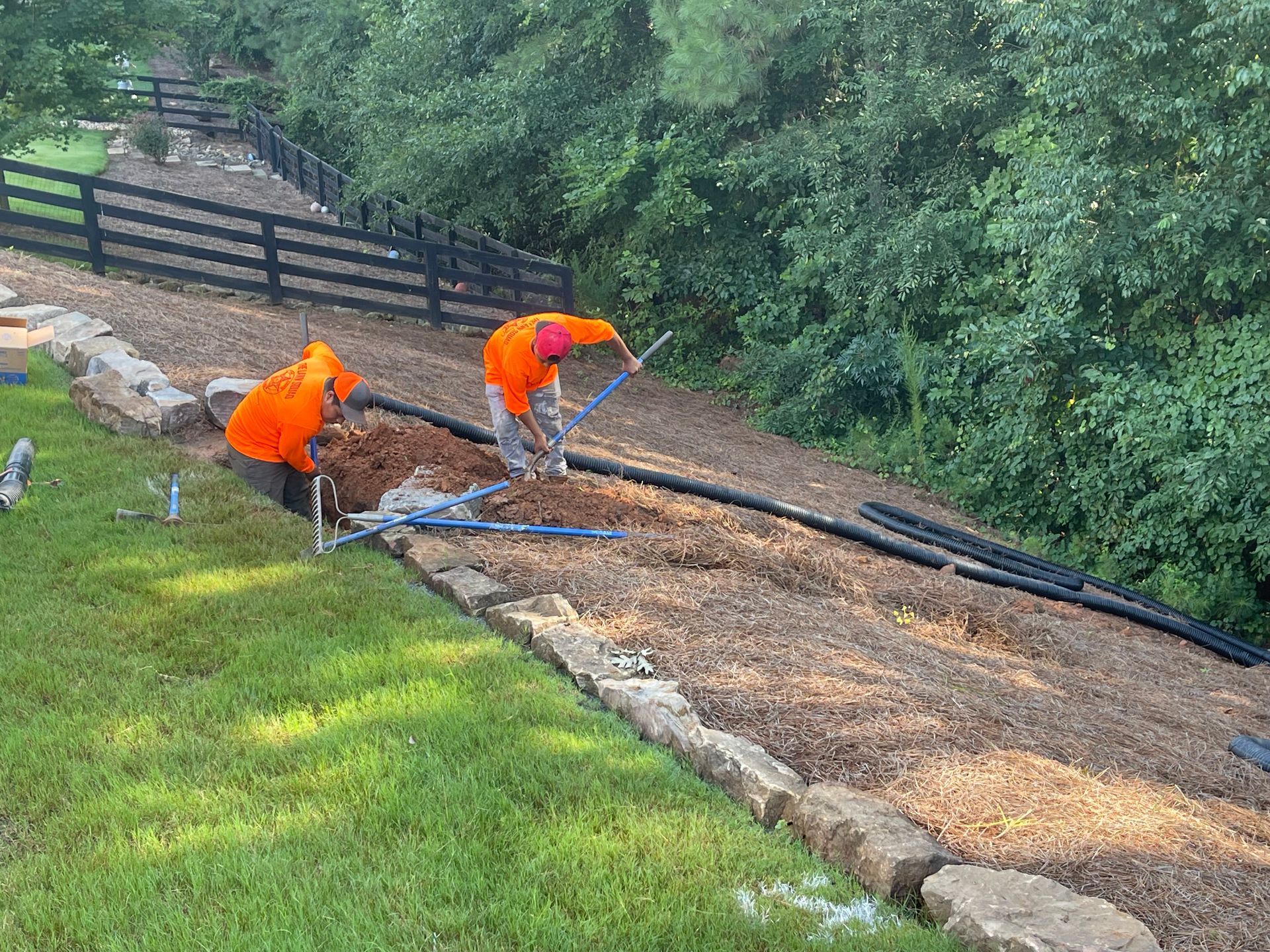 Two men are working on a dirt road next to a fence.