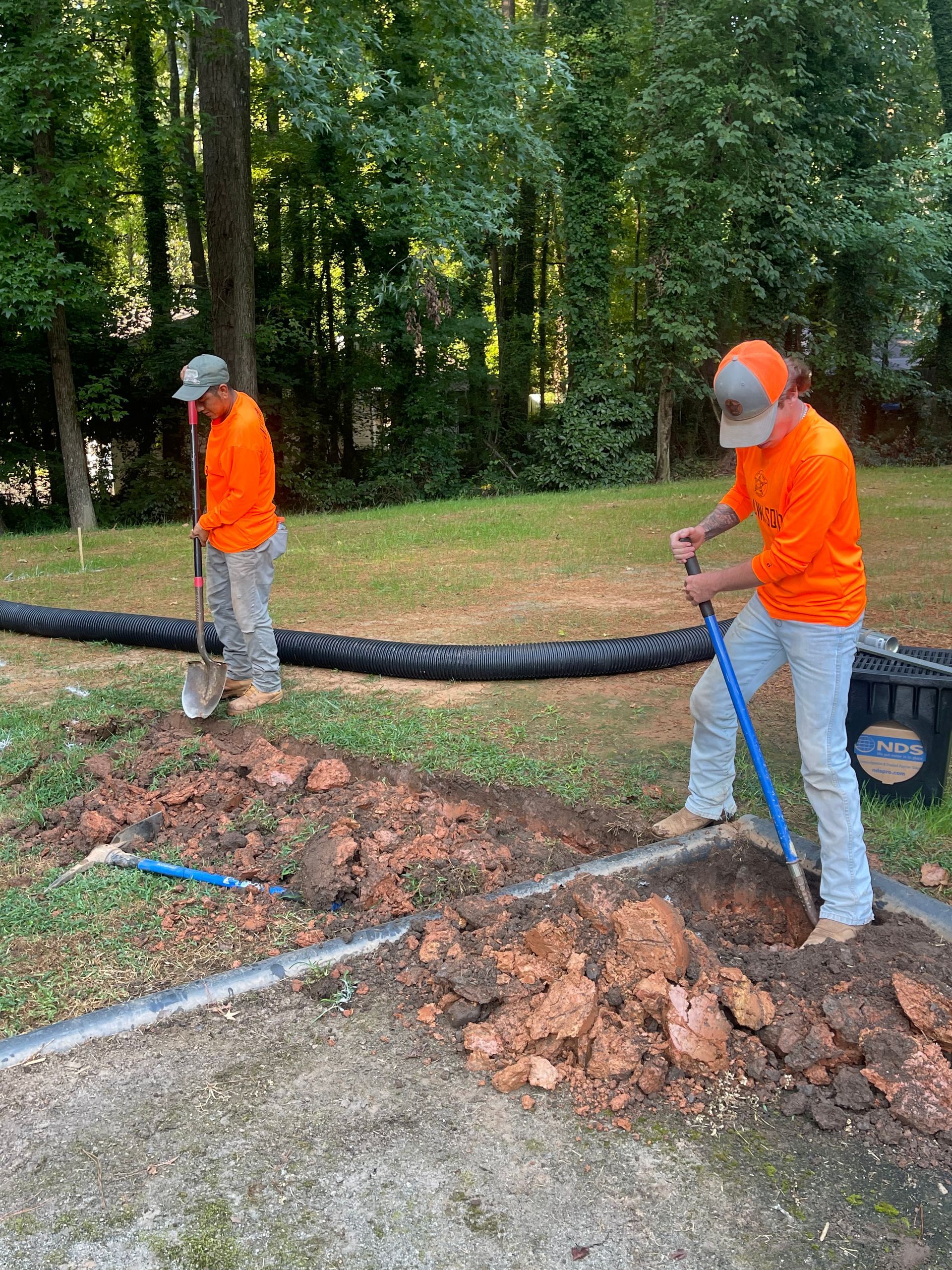 Two men are digging a hole in the dirt in a yard.