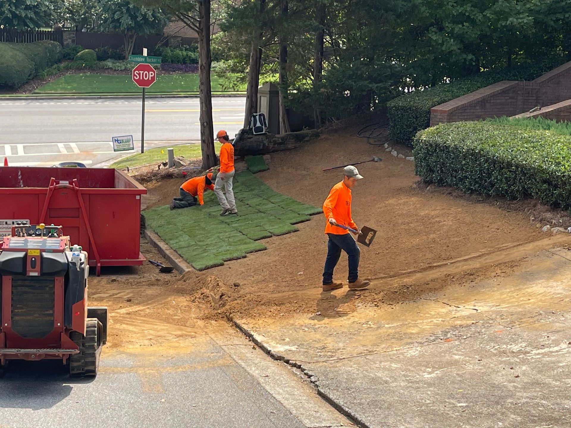 A group of men are working on a lawn in front of a stop sign.