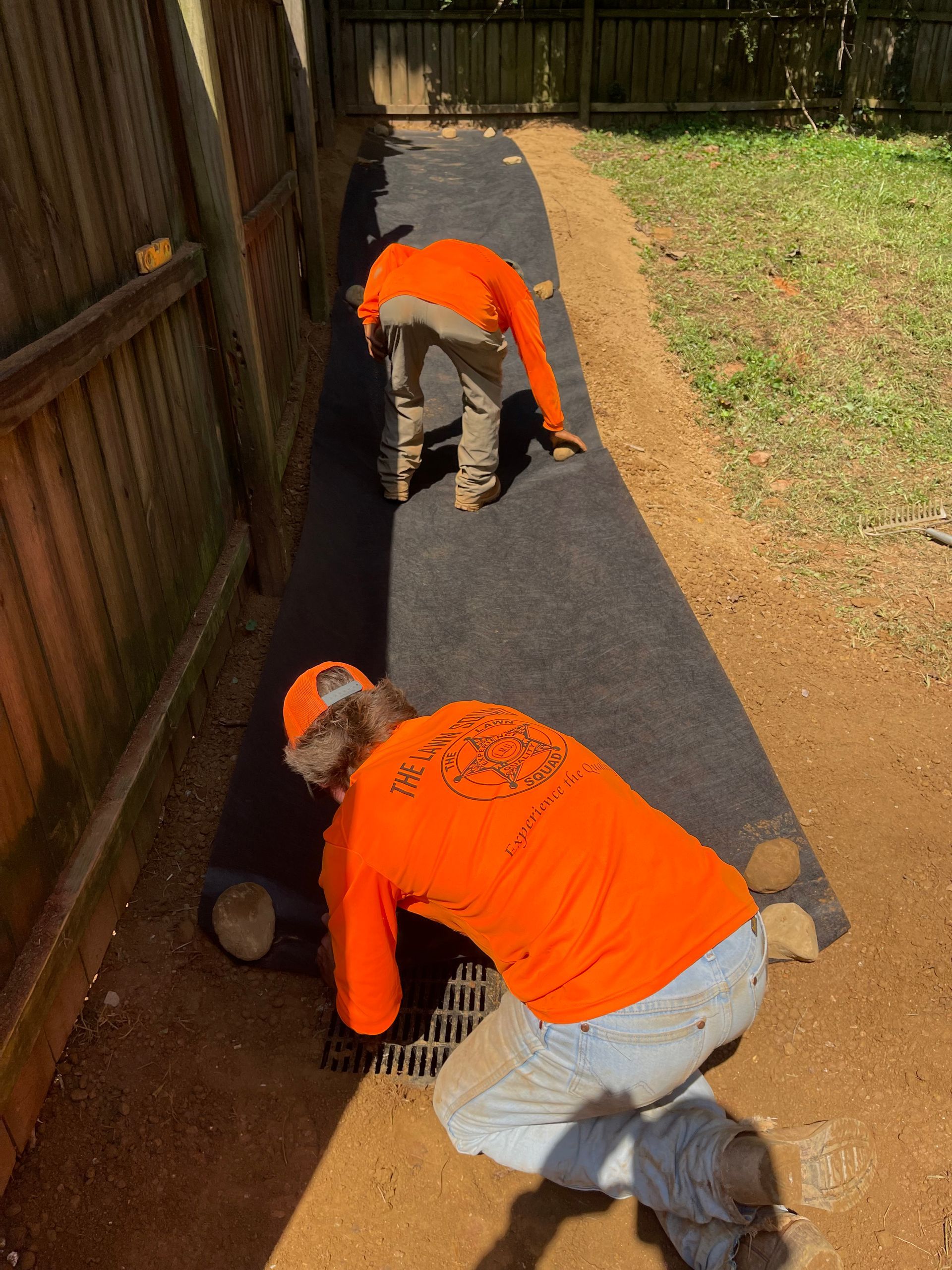Two men in orange shirts are working on a sidewalk
