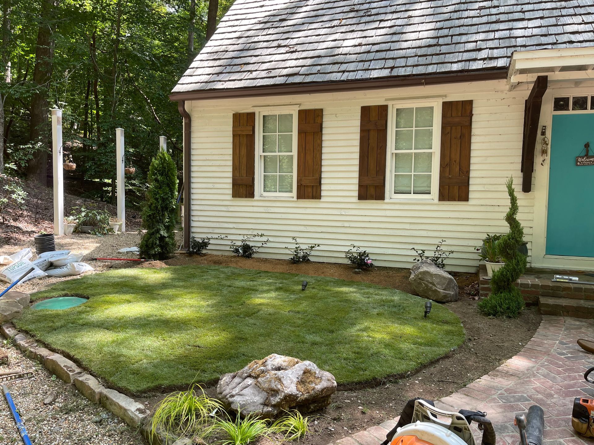 A white house with brown shutters and a blue door has a lush green lawn in front of it.