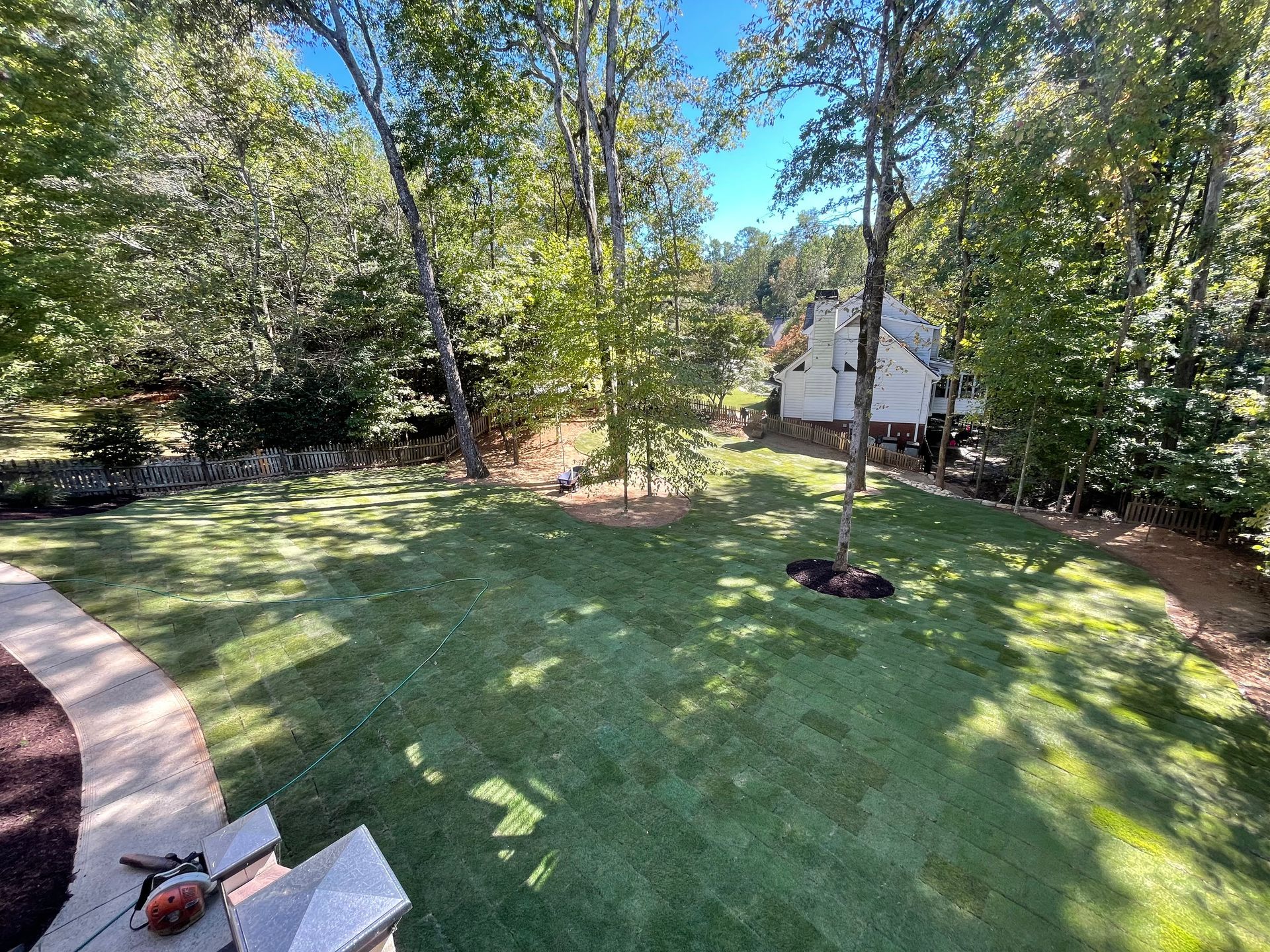 A large lush green lawn with trees and a house in the background.