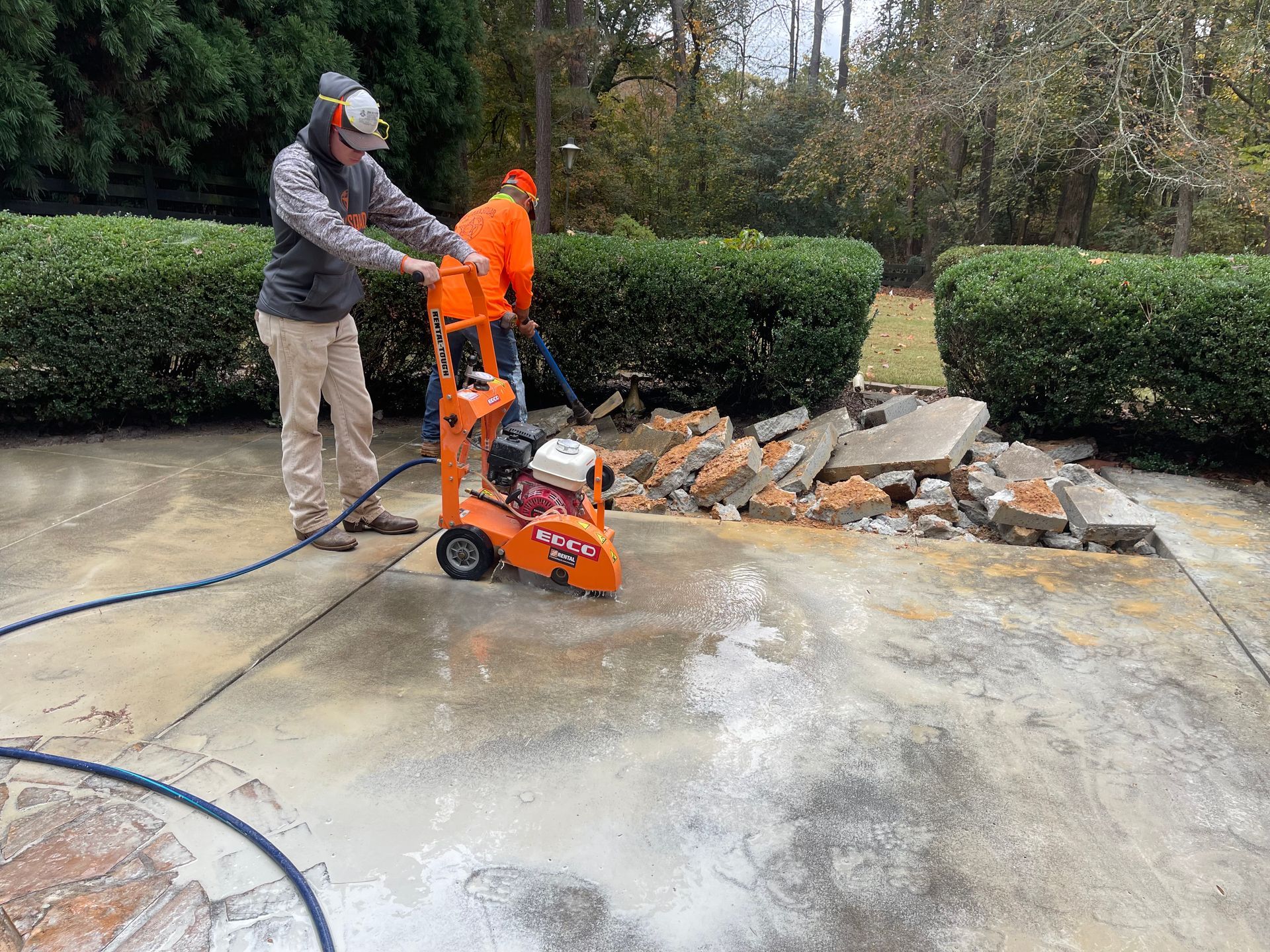A man is using a concrete saw to cut a concrete driveway.