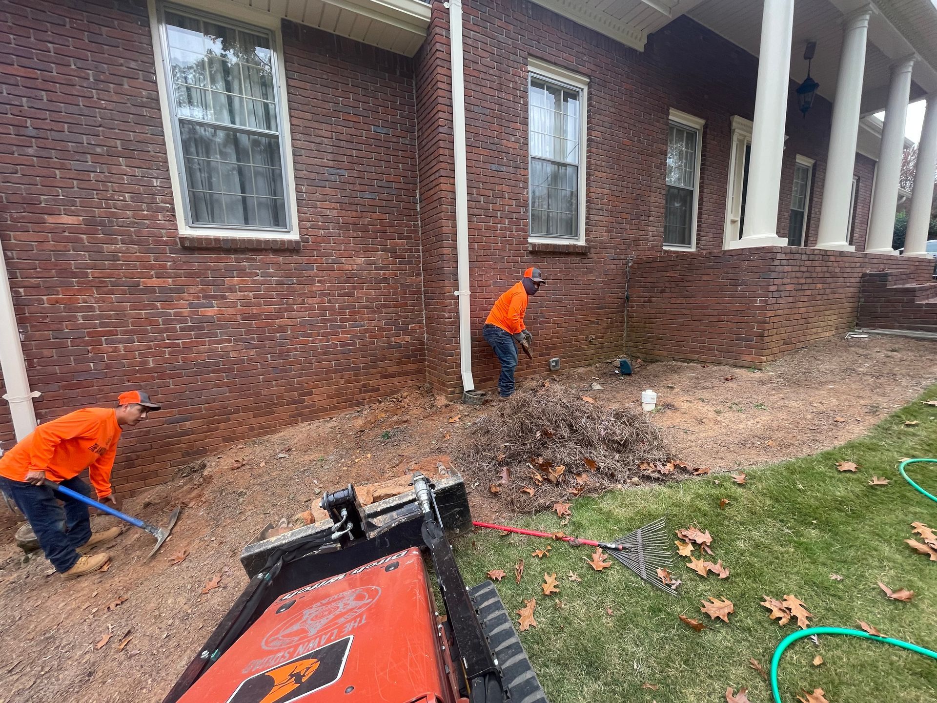 Two men are working in front of a brick house.