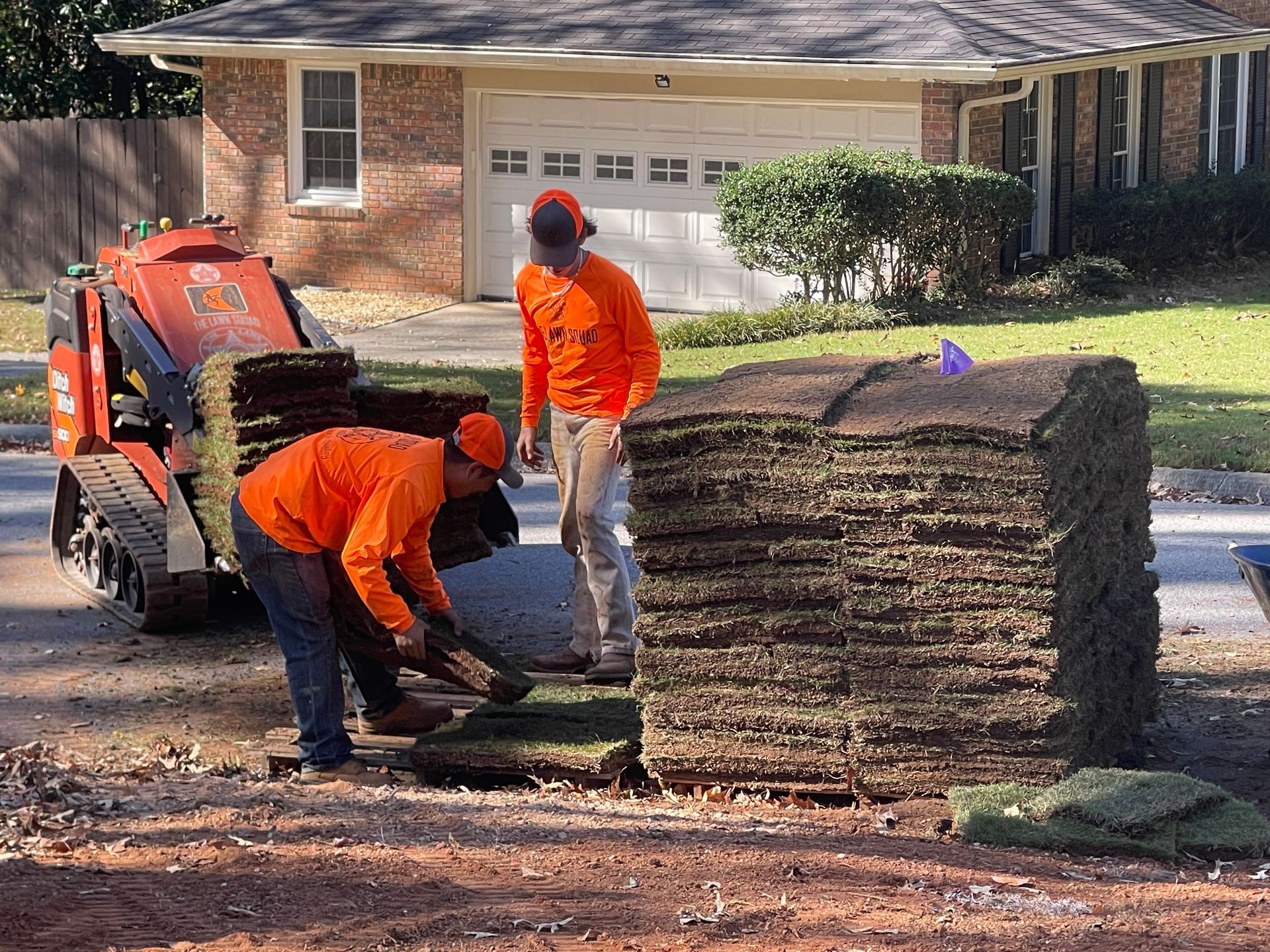 Two men are working on a lawn in front of a house.