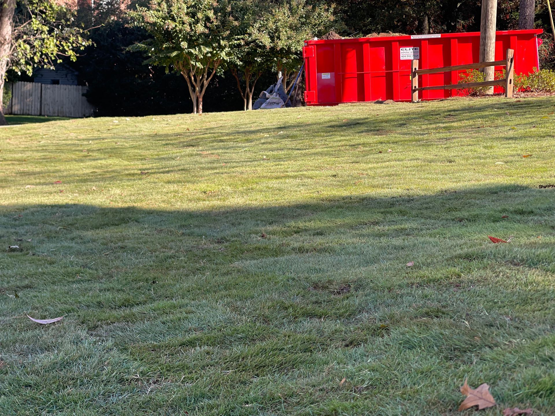 A large red dumpster is sitting in the middle of a lush green field.