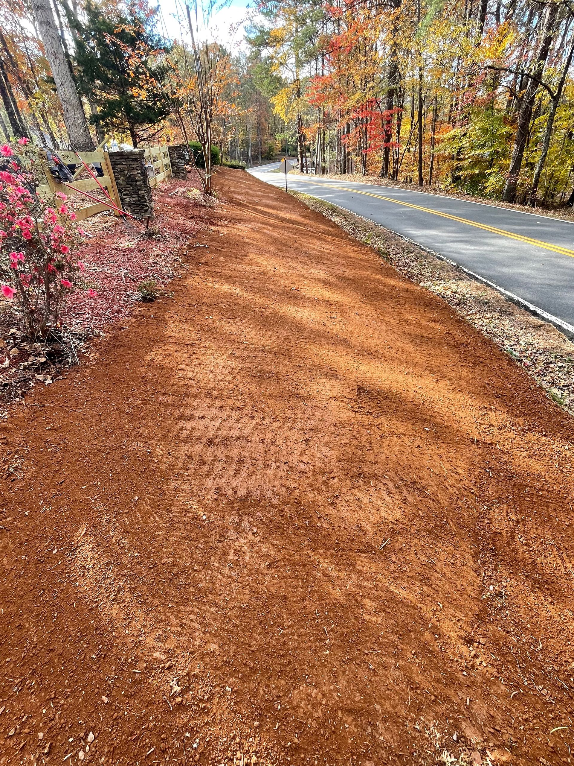A dirt road next to a road with trees on the side of it.